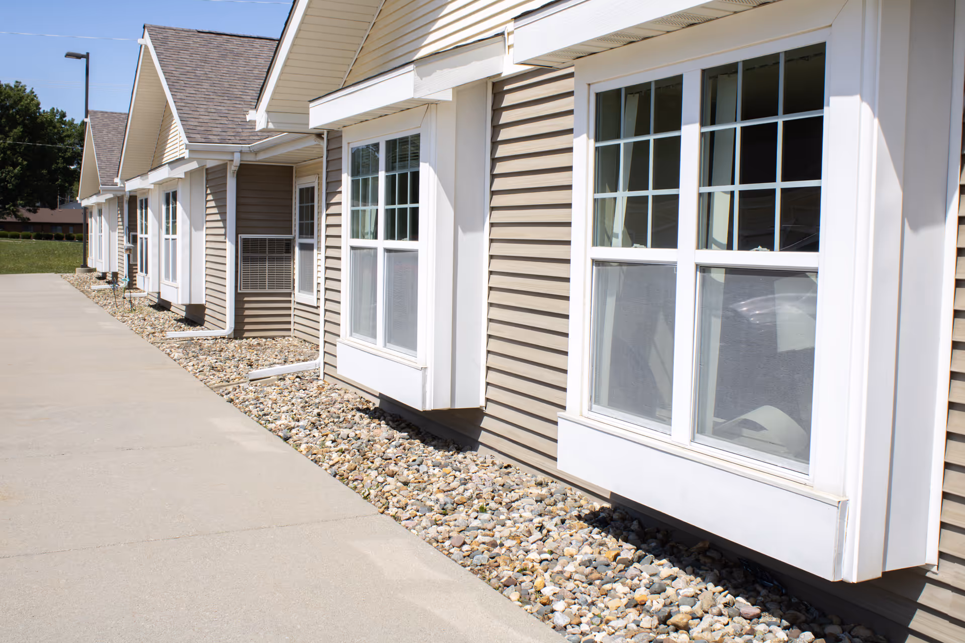 Row of beige senior living cottages with white-trimmed windows along a rocky landscape.