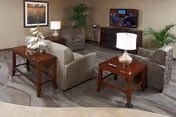 A cozy senior living lounge with sofas, tables, lamps, and a wall-mounted TV.