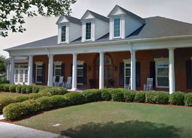 Exterior view of a brick senior living building with a covered porch and rocking chairs.