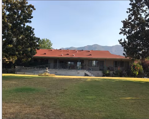 Single-story building with a red roof and covered porch overlooking a wide grassy lawn with mountains in the background.