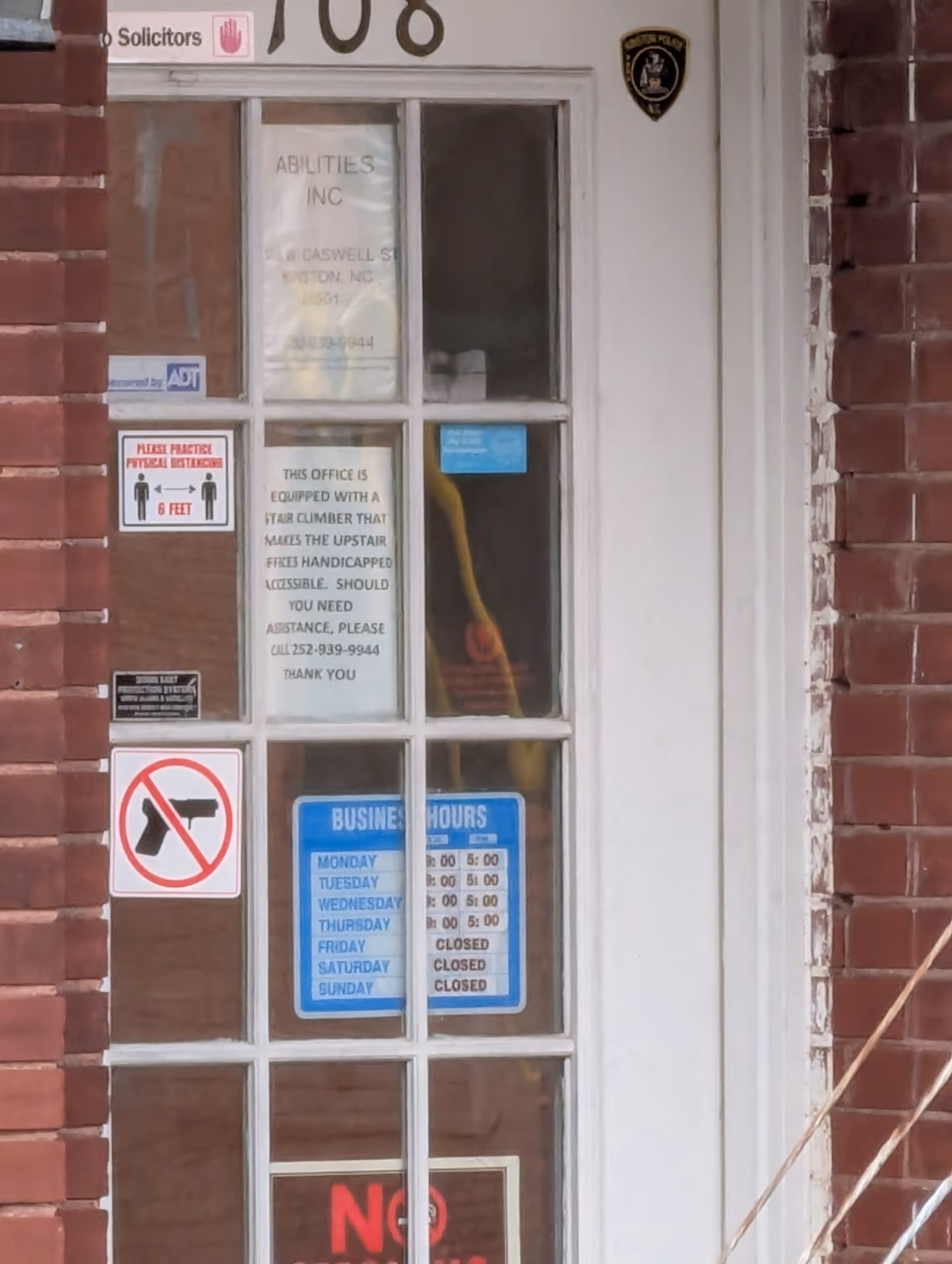 Brick exterior building entrance with glass door displaying Abilities Inc signage and posted notices.