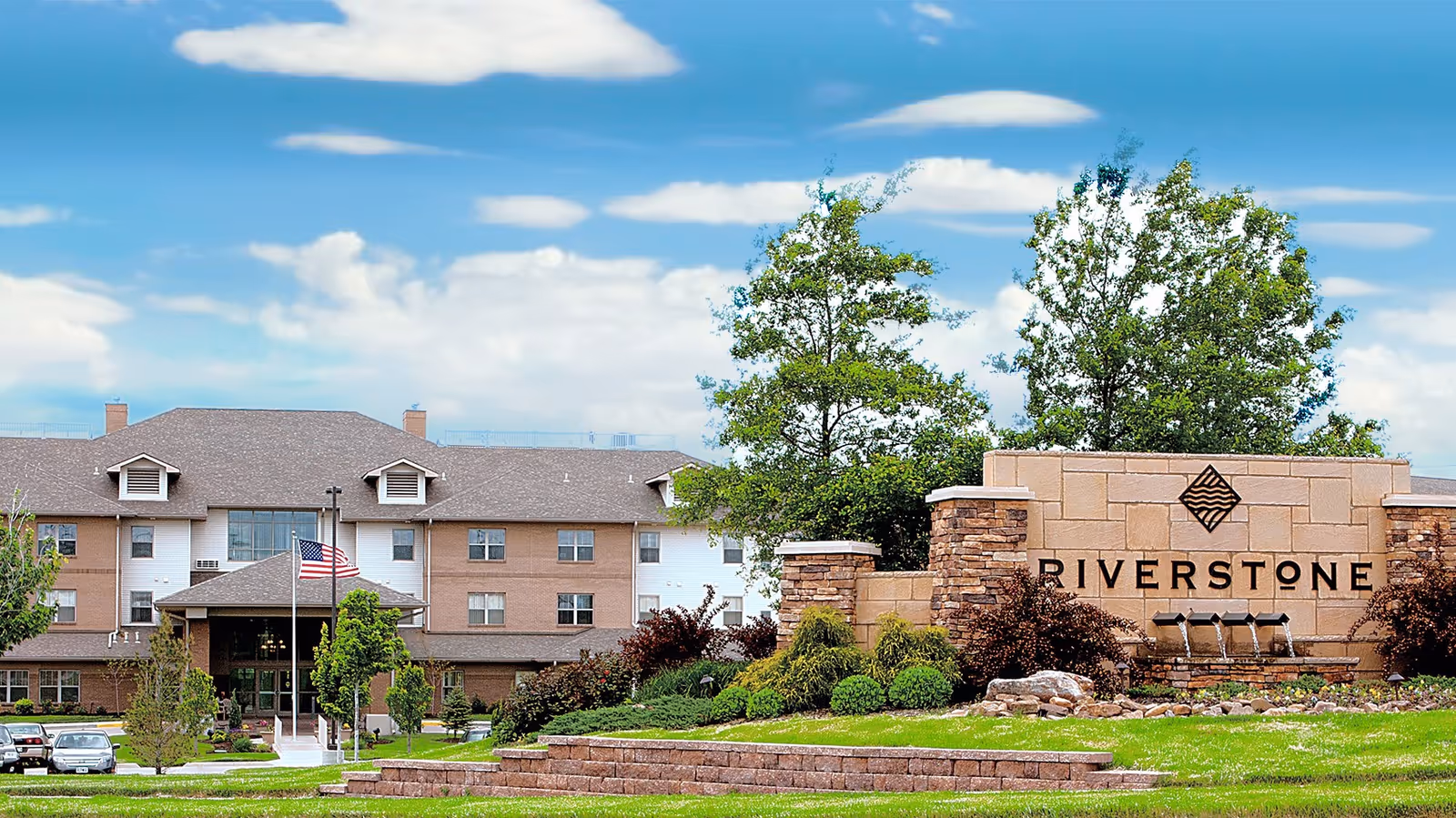 Exterior view of Riverstone Retirement Community with entrance, landscaped grounds, and a large sign.