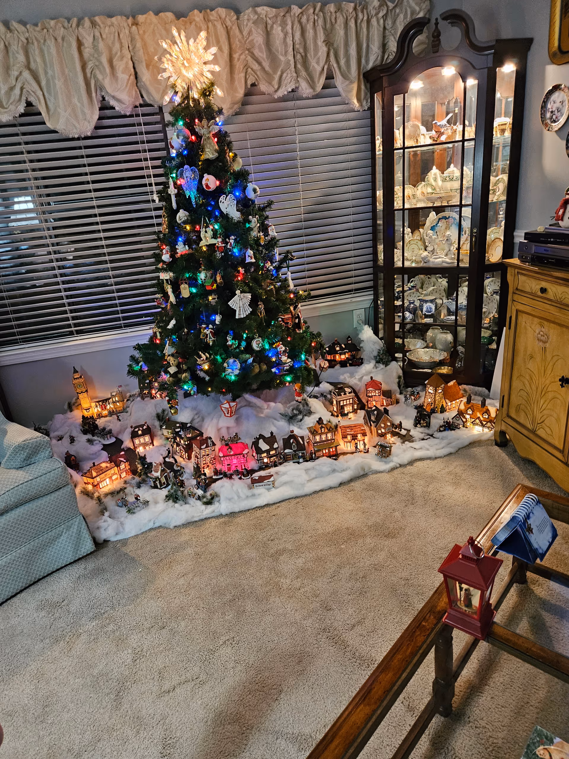 A decorated Christmas tree with miniature houses along snowy base in a cozy living room.