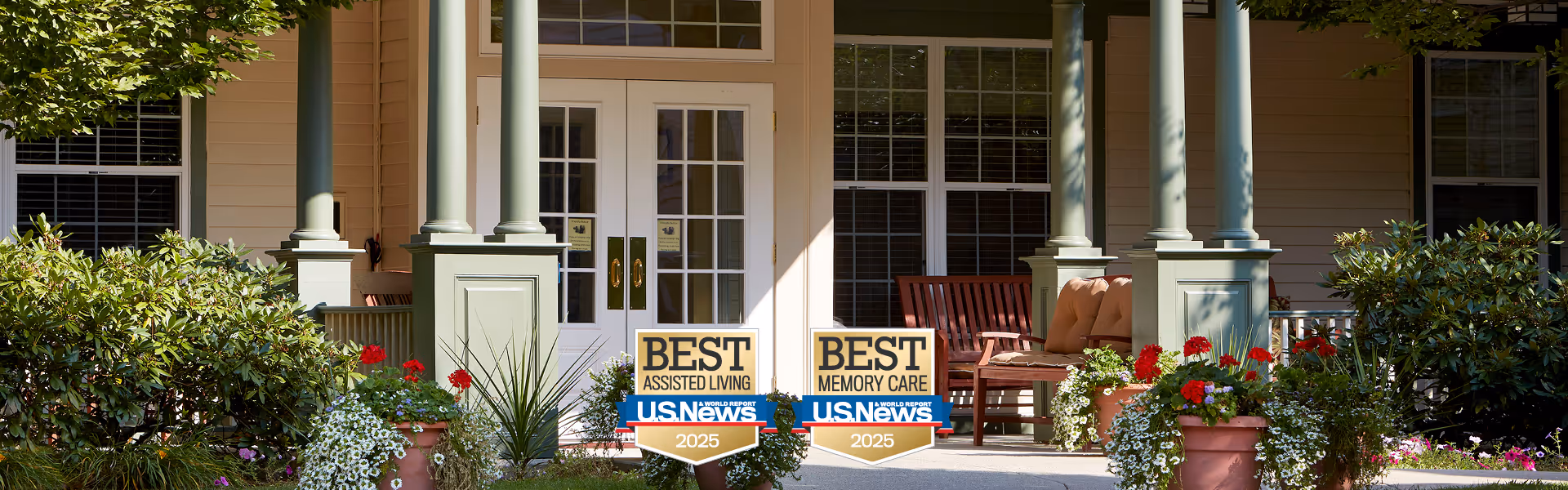 Front porch entrance of Benchmark at Tatnuck Park with chairs, potted flowers, and two 'Best' US News 2025 award signs for assisted living and memory care.