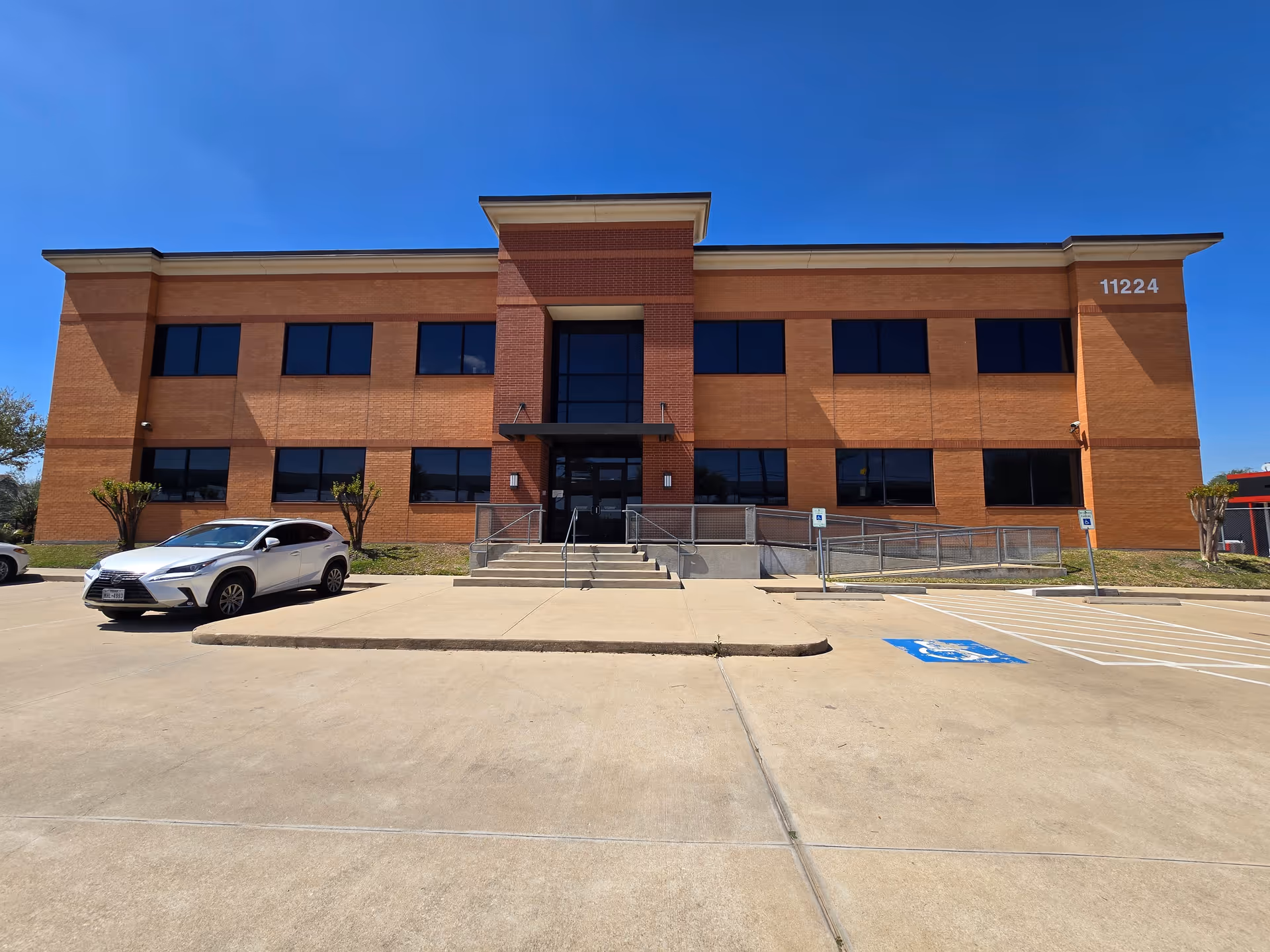 Brick senior living facility front entrance with stairs, parking, and blue sky.