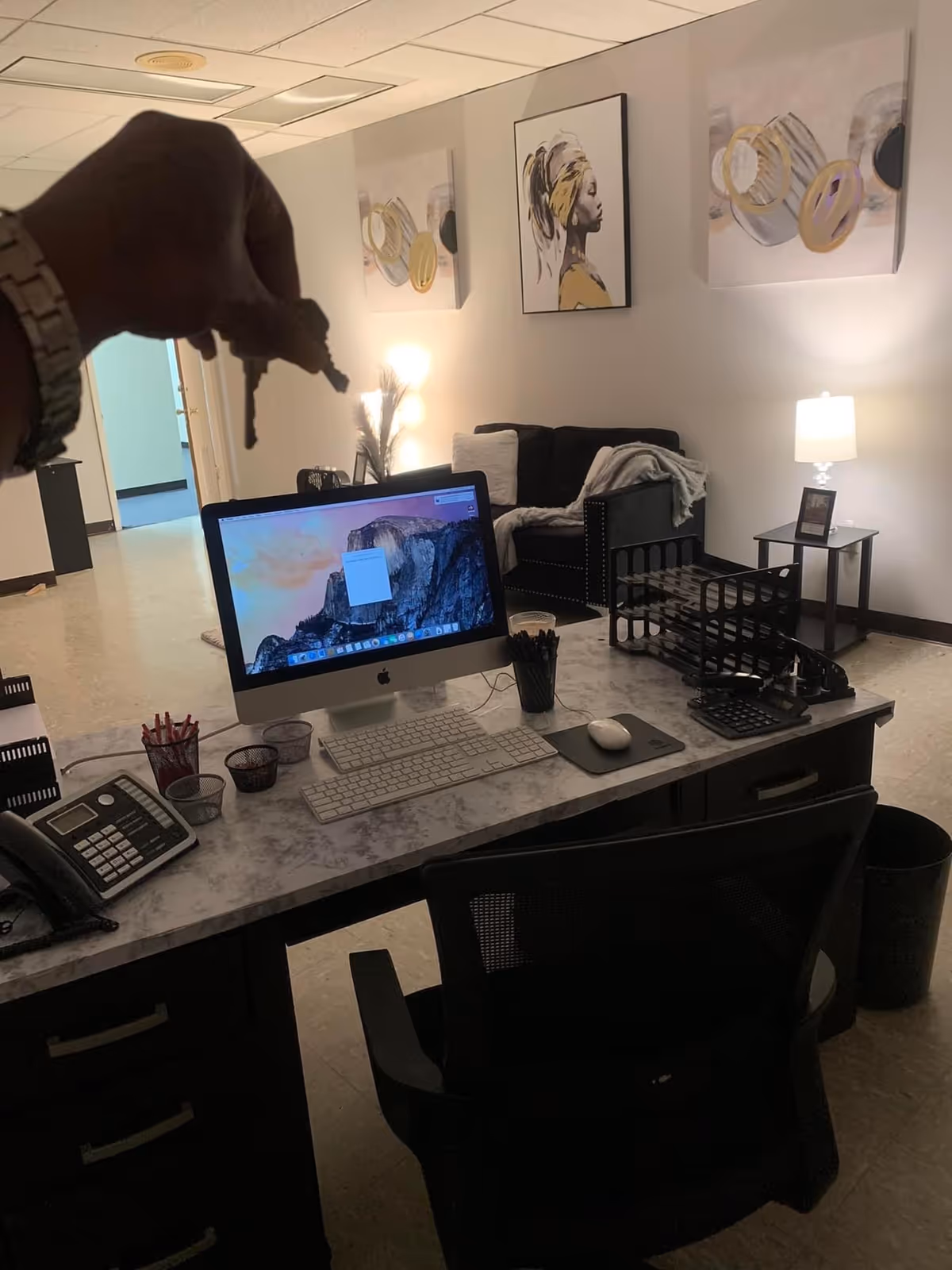 Desk with computer and keyboard; a hand holds a key, living area with couch in background.