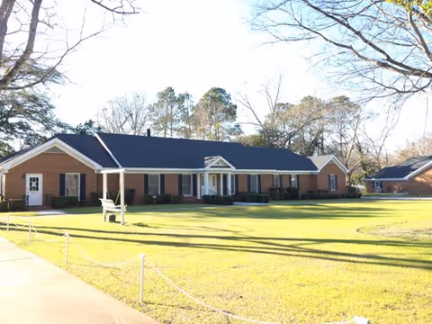 A brick, single-story senior living facility front with a manicured lawn and trees.