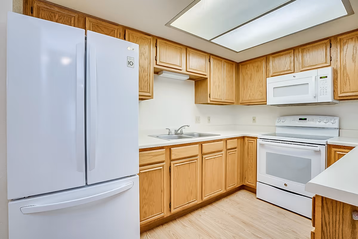 Bright kitchen with white appliances, wooden cabinets, sink, microwave, and stove.