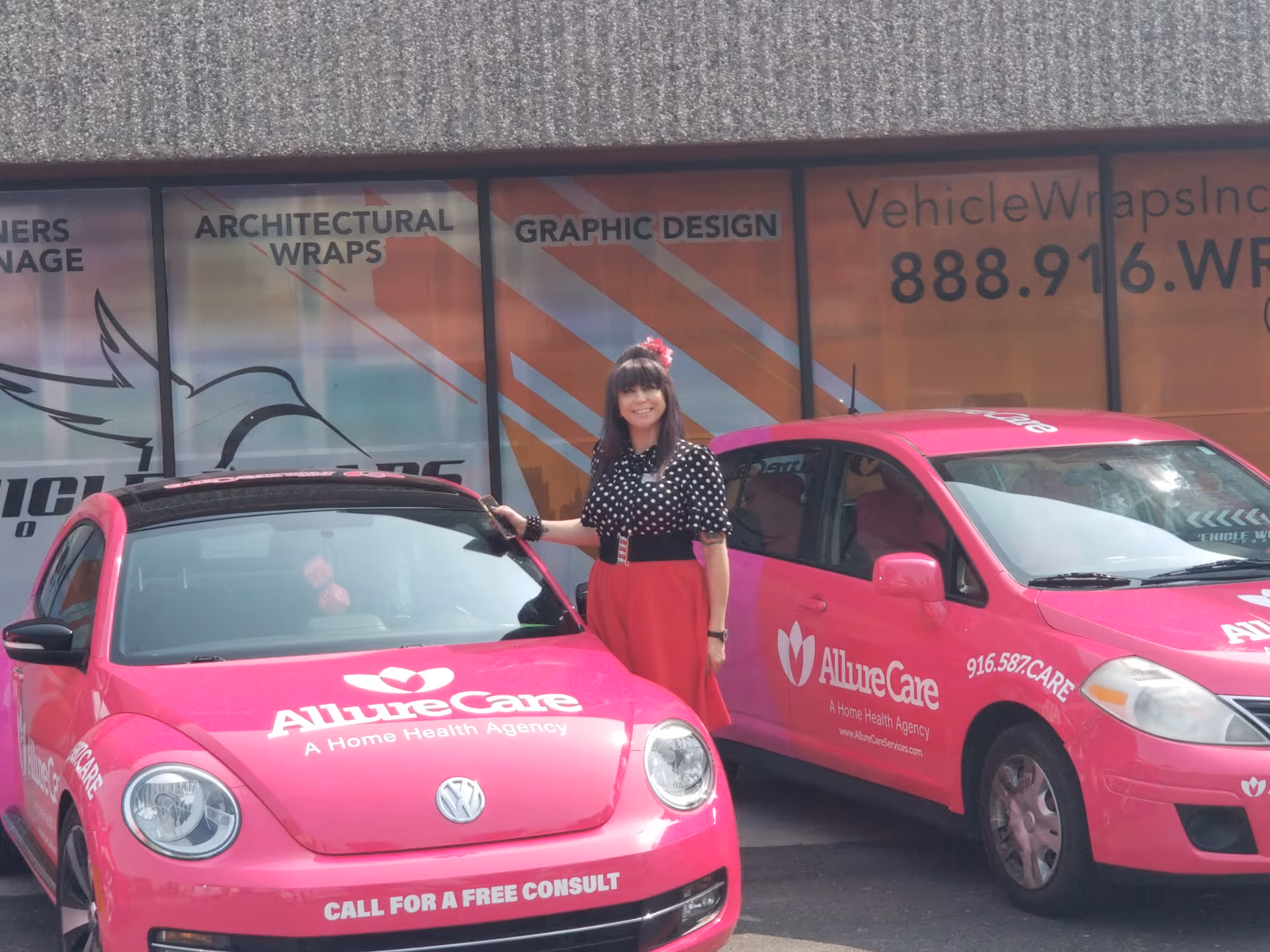 A woman stands between two bright pink AllureCare vehicles parked outside a building.