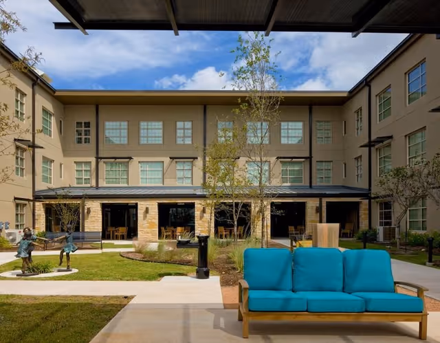 Outdoor courtyard of Elan Southpark Meadows with turquoise sofa, trees, and a beige building.