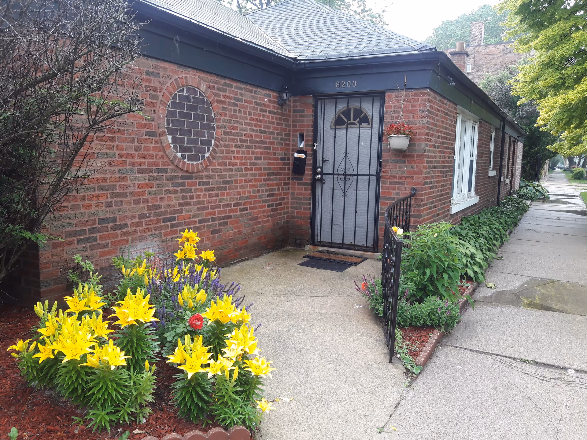 Brick building exterior with a metal front door, arched window, and colorful flowers.