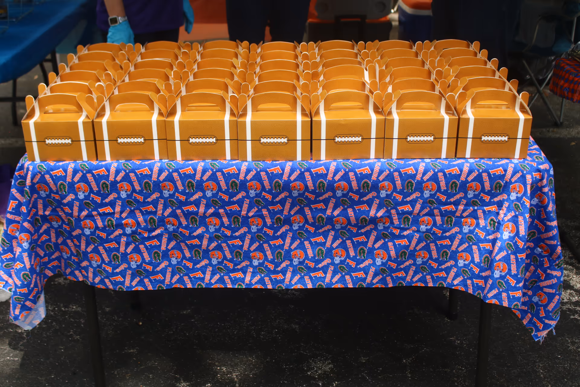Table outdoors displays numerous orange lunchboxes atop a blue patterned tablecloth.