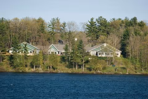 Lakeside Boardman Lake Glens buildings with green roofs sit among trees beside a blue lake.