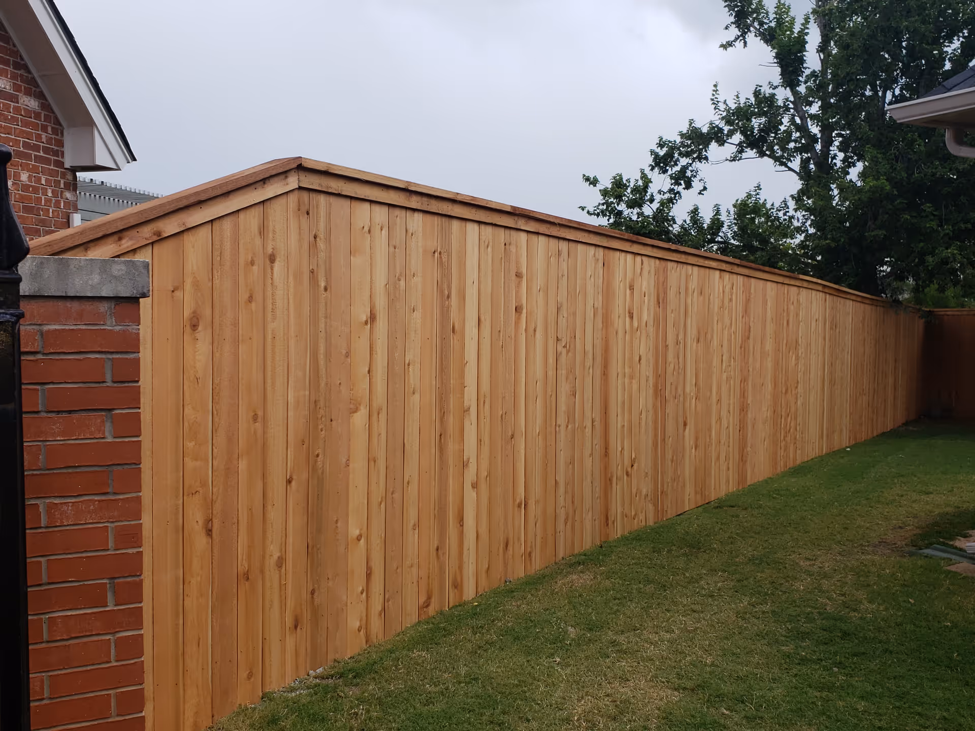 Long wooden privacy fence runs along a grassy side yard beside a brick house.