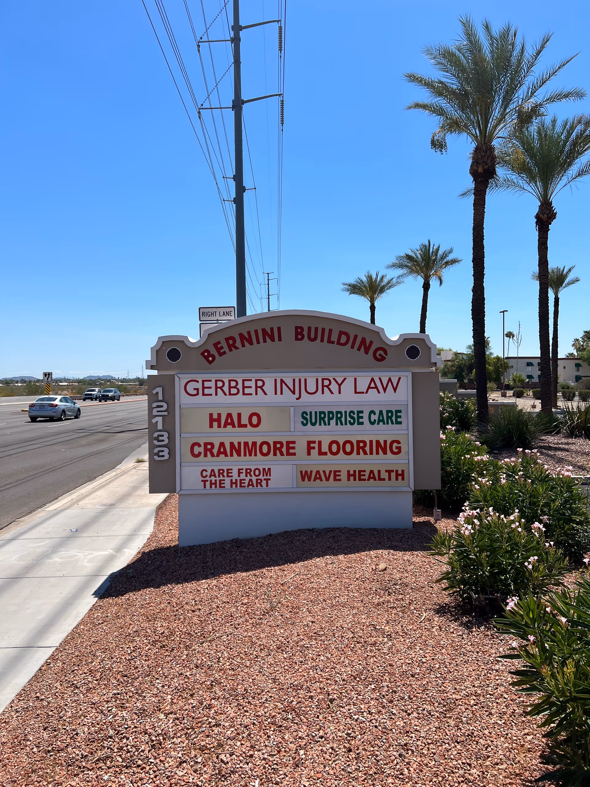 Exterior sign for Bernini Building listing Surprise Care among tenants, with palm trees nearby.