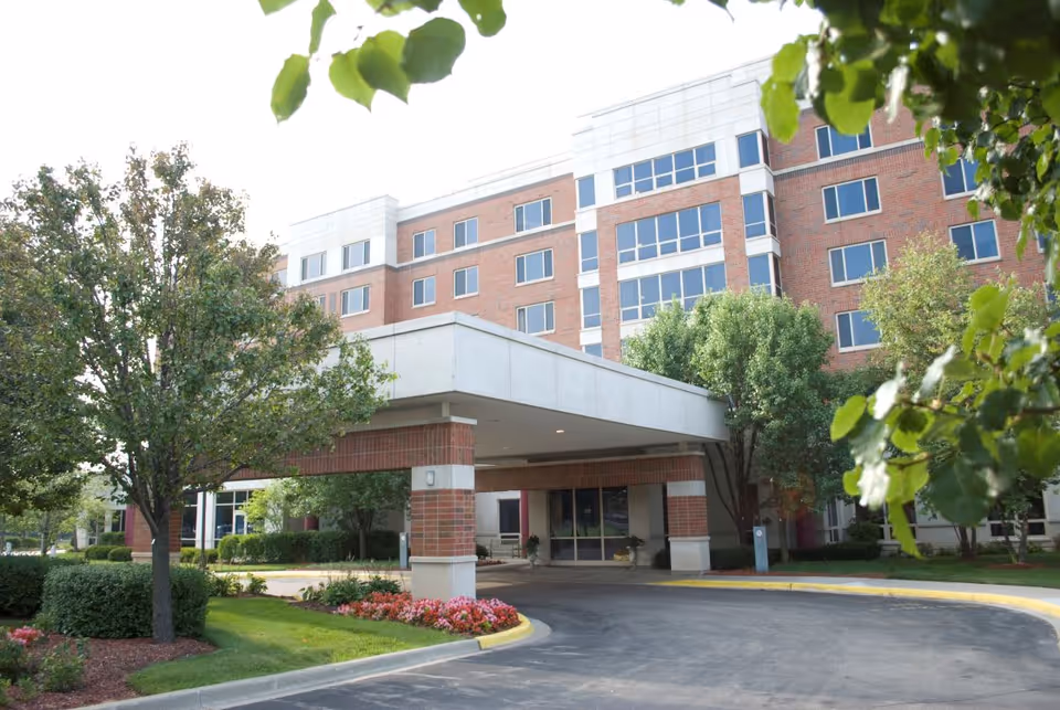 Brick senior living building with a covered entrance and manicured landscaping.