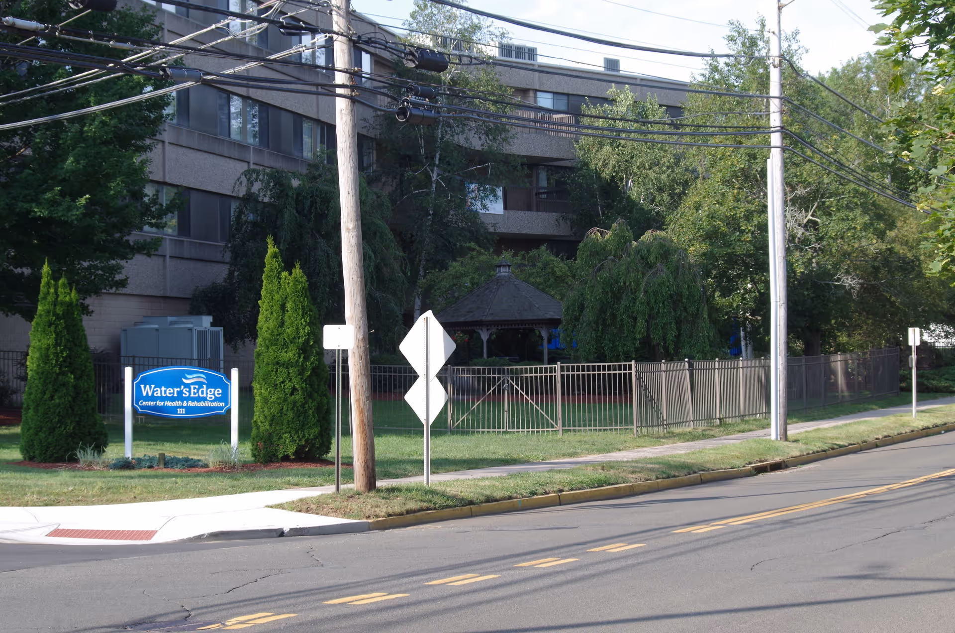 Exterior view of Water's Edge Center for Health and Rehabilitation; sign, fence, and gazebo on lawn.