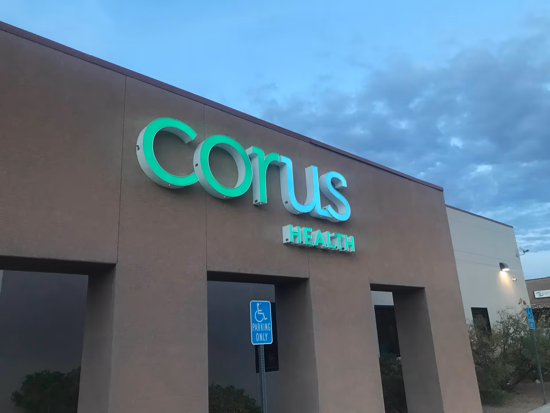 Facade of Corus Health building with green and blue sign on exterior wall.