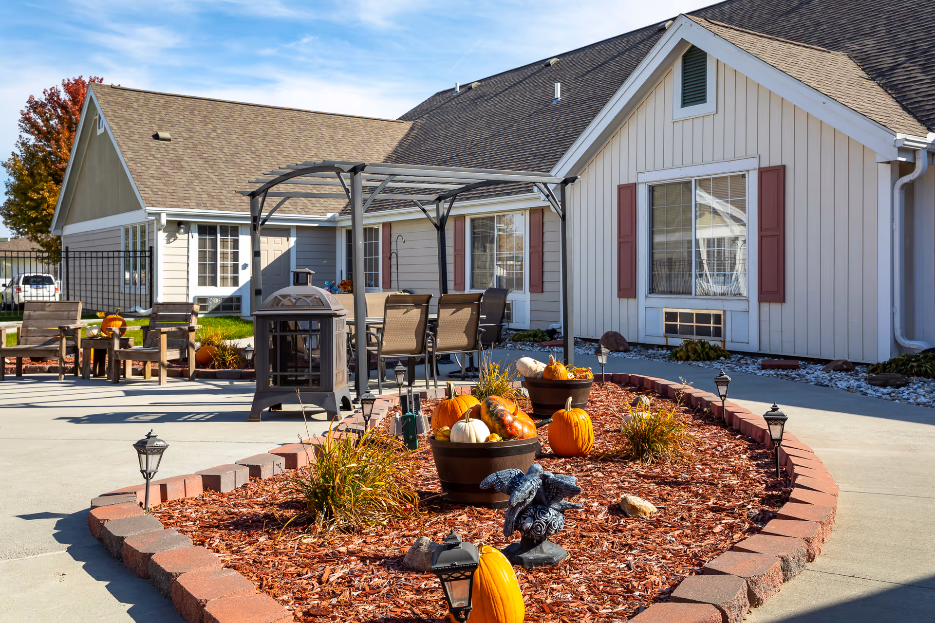 Outdoor courtyard and seating area in front of a single-story assisted living building decorated with pumpkins and landscaping.