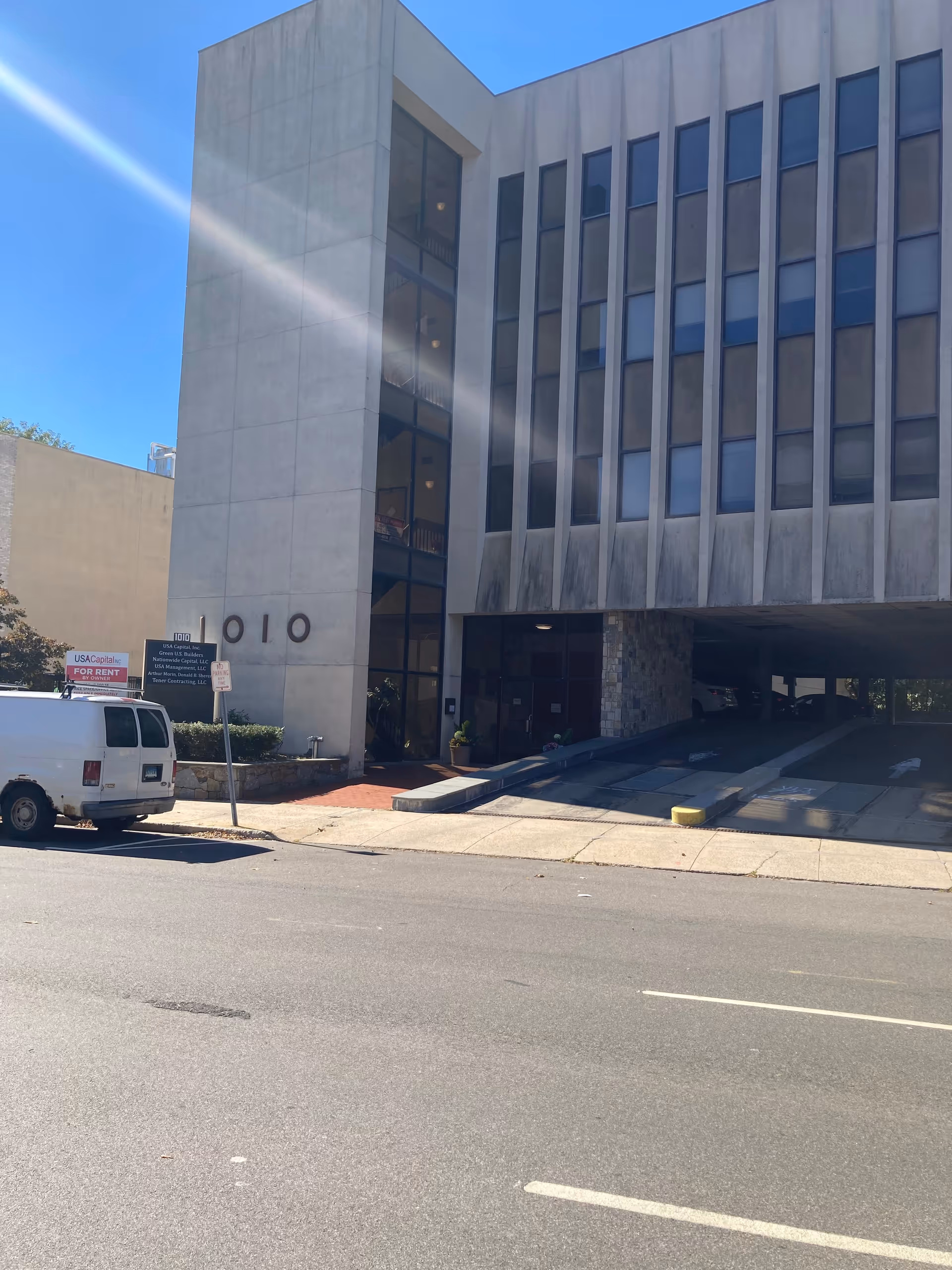 Modern multi-story building exterior with large windows, a ramp, and a white van on the street.