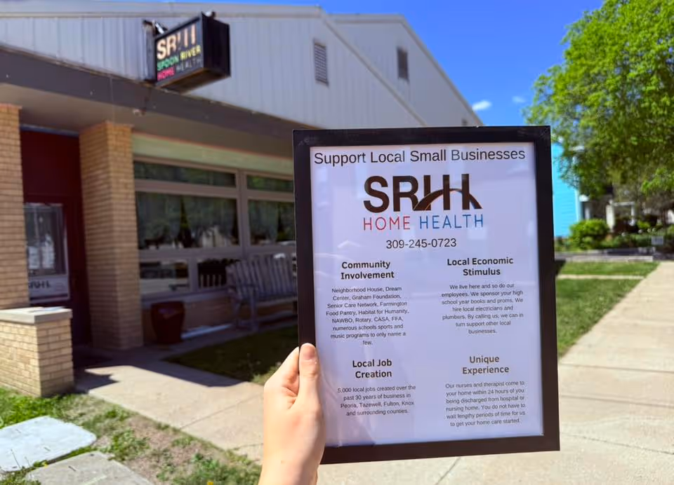 A hand holds a framed sign in front of a Spoon River Home Health Services building.