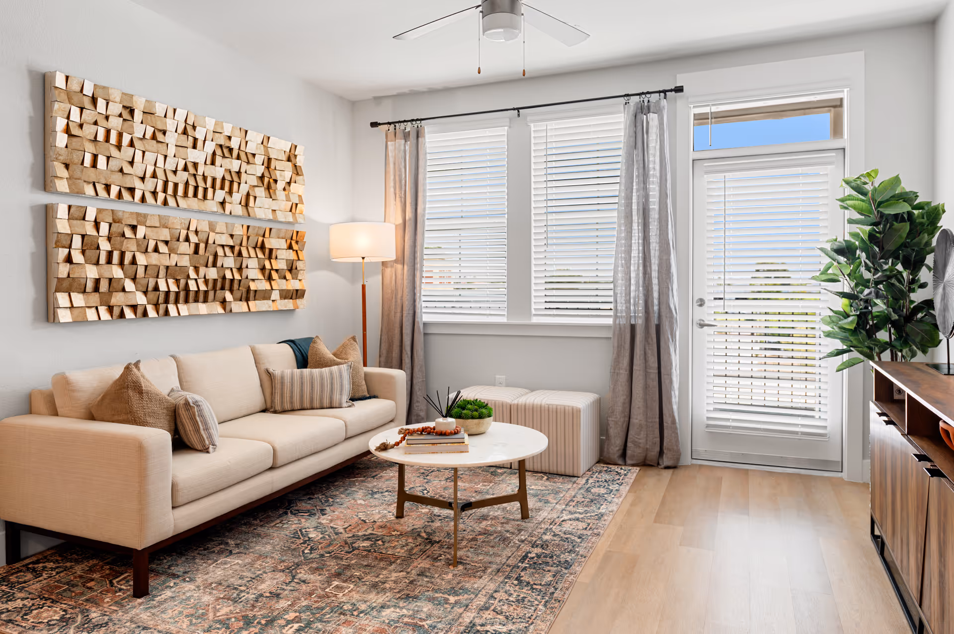 Bright living room with beige sofa, wall art, rug, windows, and potted plant.