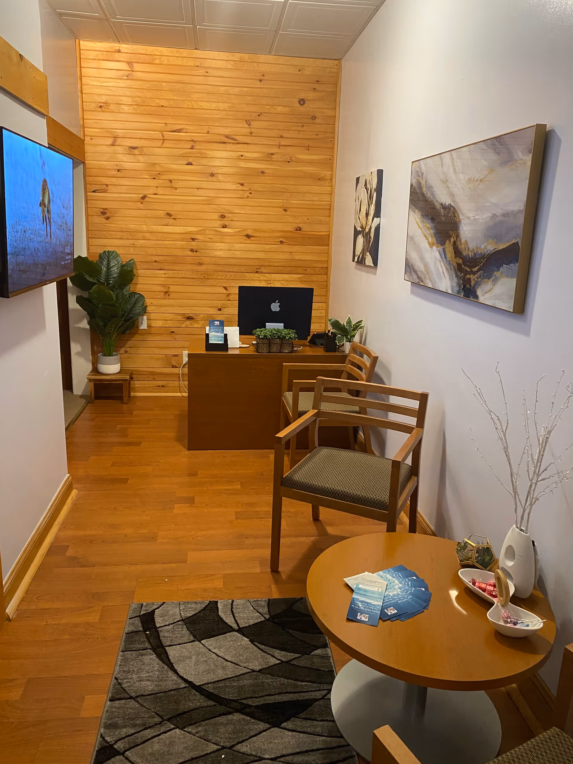 Reception area with wooden panel wall, desk, chairs, plants, and artwork.