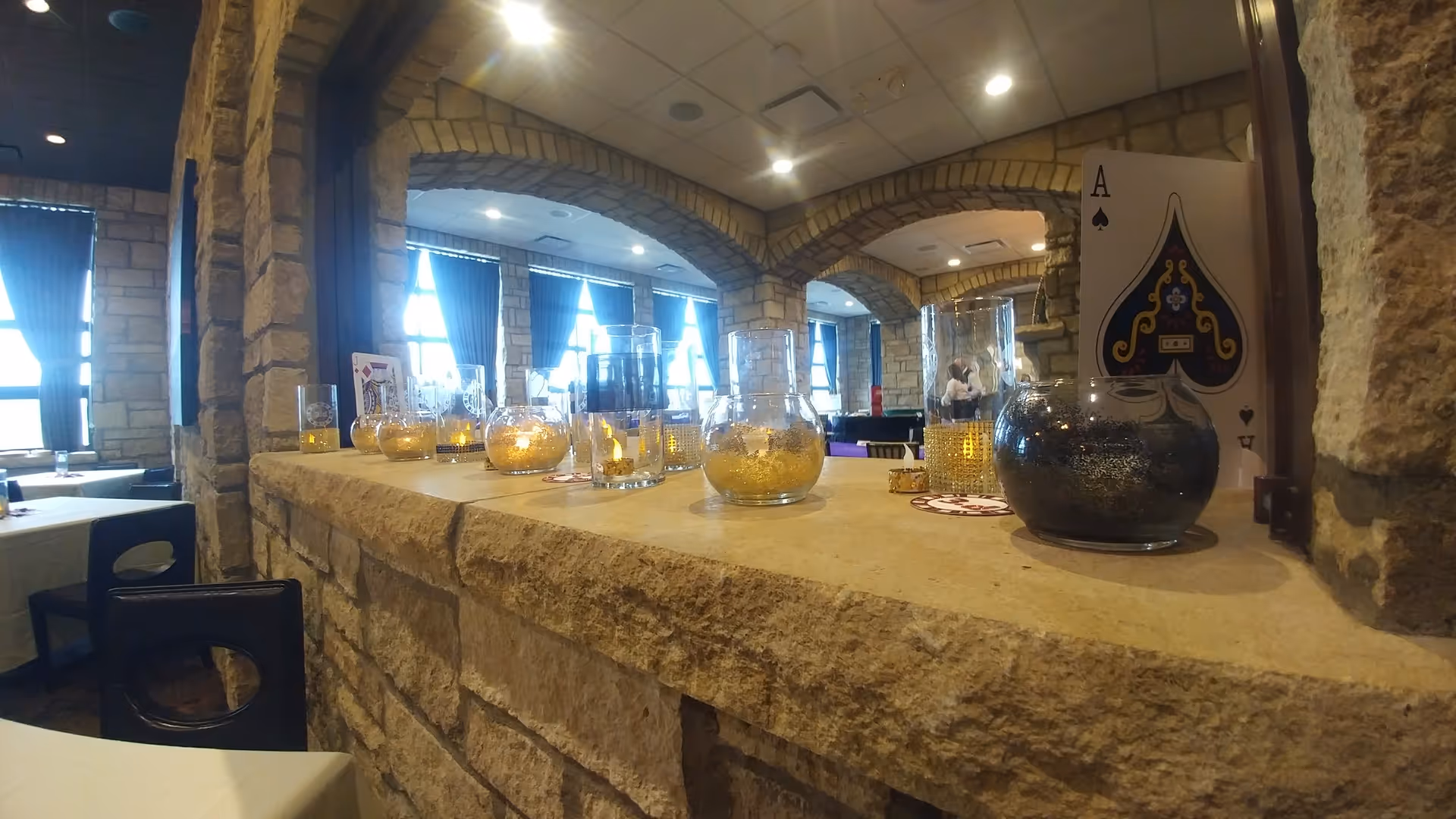 Stone bar counter indoors with glass jars and a playing-card prop in a stone dining area.