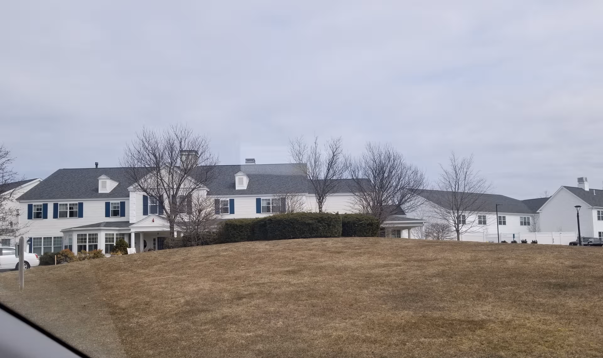 Long, white senior living facility with blue shutters sits on a grassy, bare hill.