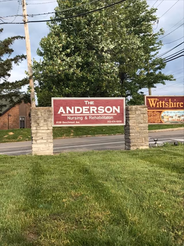 Outdoor view of a sign for The Anderson Nursing & Rehabilitation Center mounted on two stone pillars with a grassy area in the foreground and trees and power lines in the background.