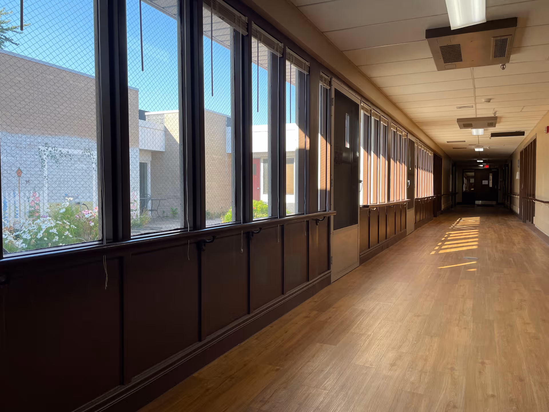 Long interior hallway of a senior living facility with large windows along one side.