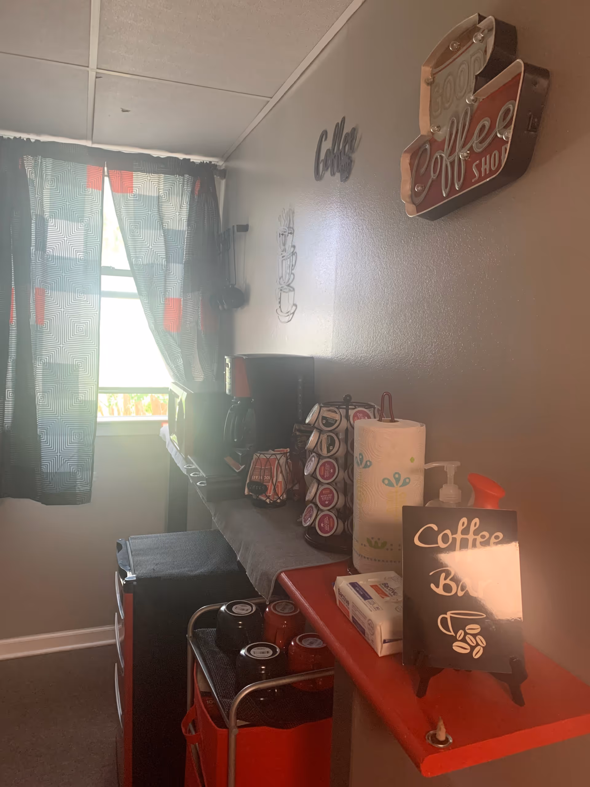Small interior coffee station with machine, cups, paper towels, and a red cart.
