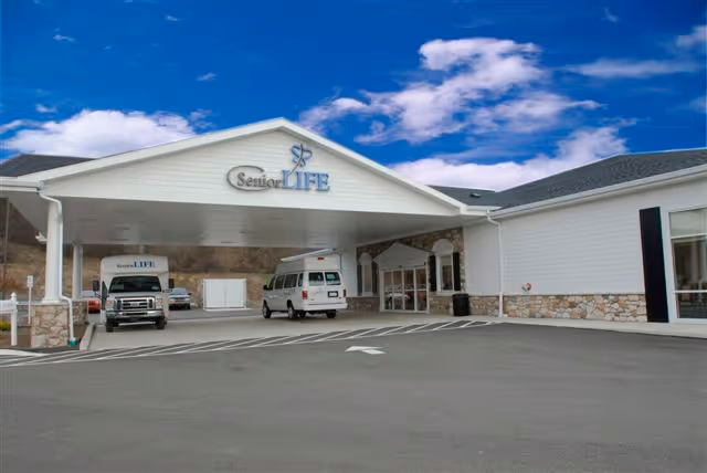 Exterior view of Senior LIFE Reading facility with a covered entrance and parked vans.