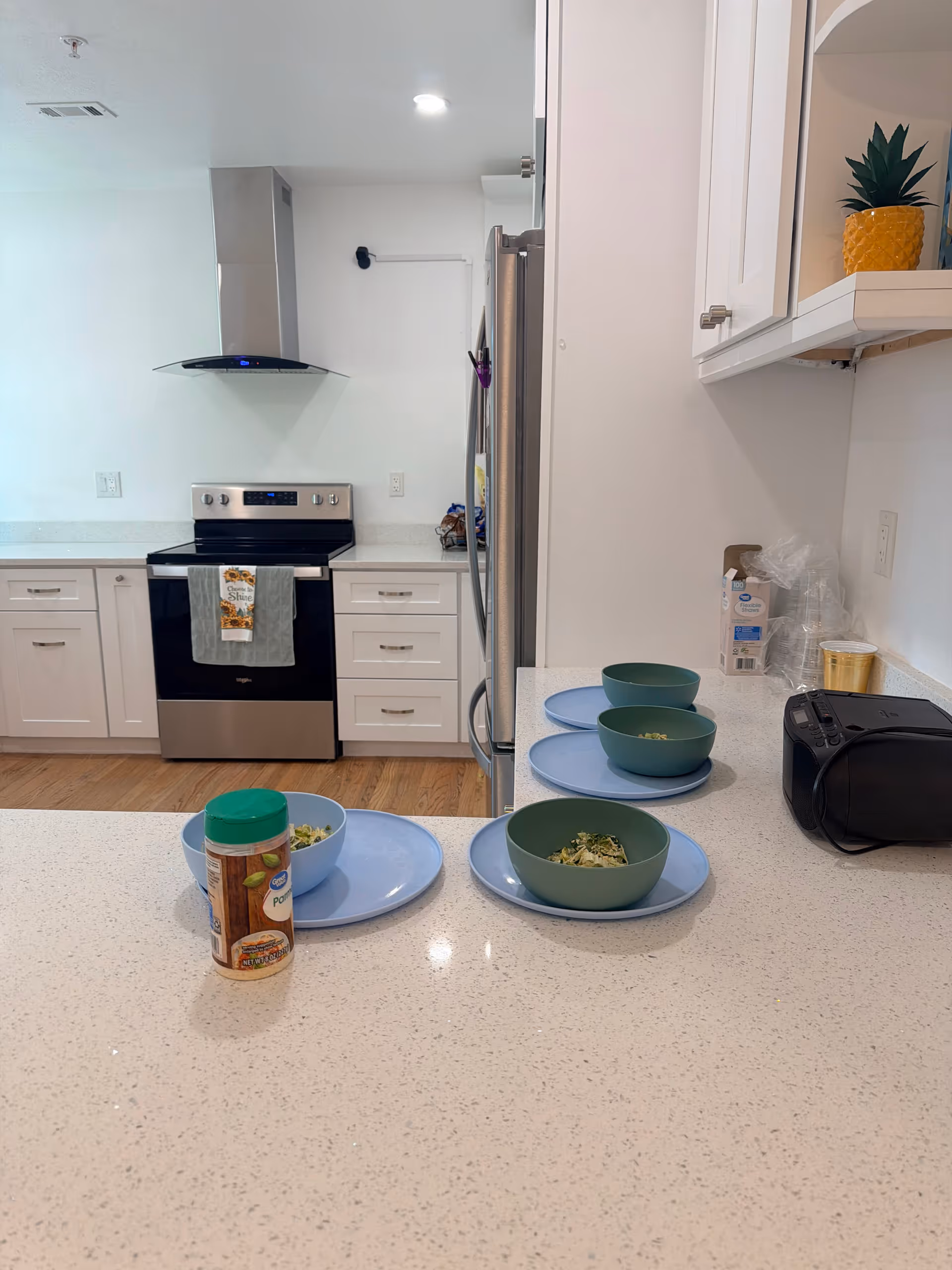 Modern white kitchen with stainless steel stove, range hood, and bowls of food on counters.