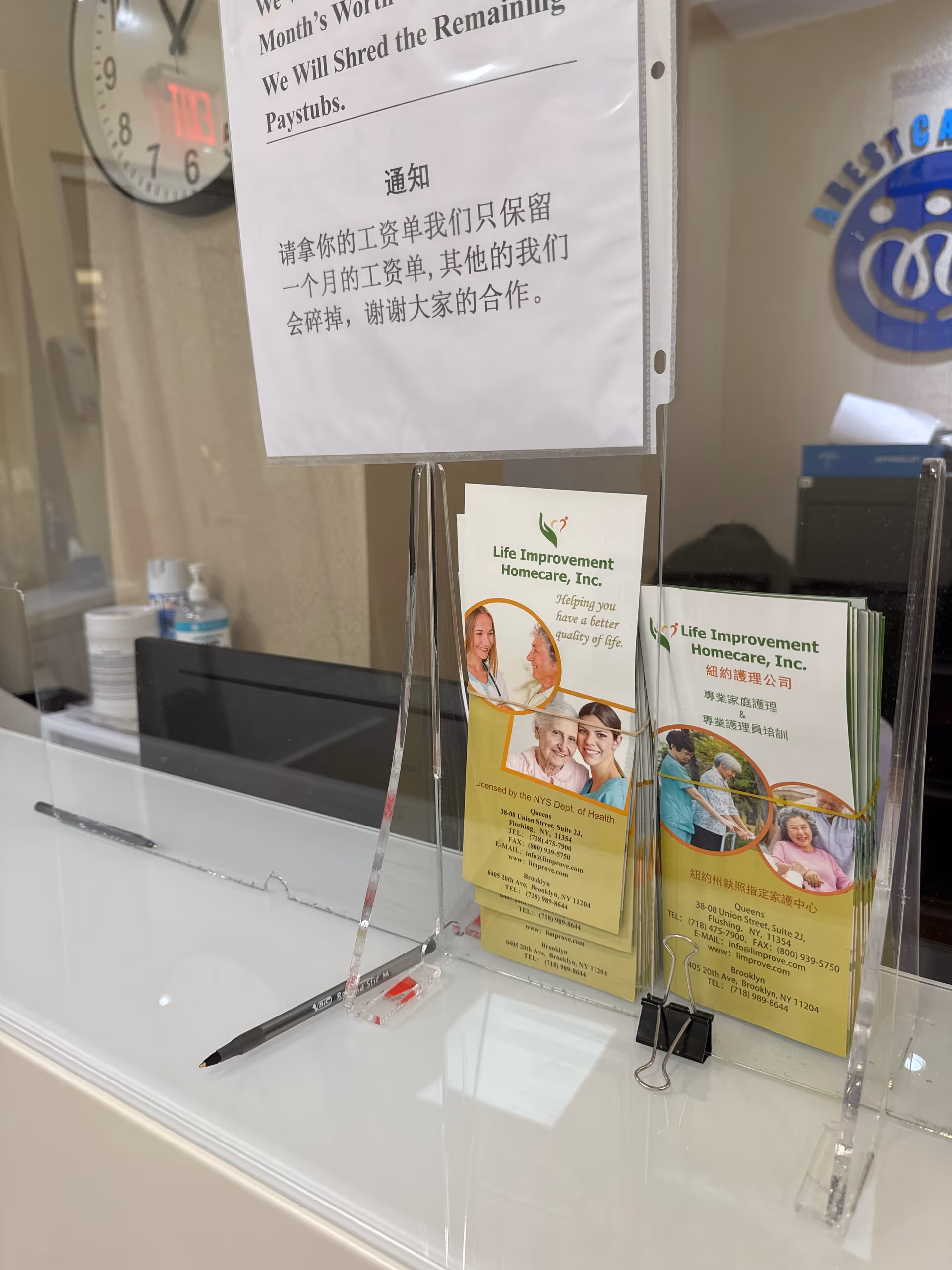 Indoor reception area with brochure stands, a clock, and a glass divider at Life Improvement Homecare.
