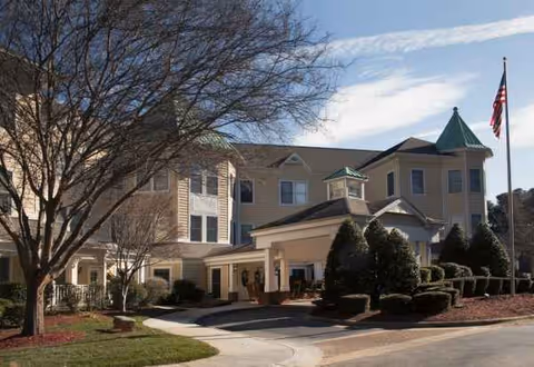 Front exterior of Sunrise of Raleigh senior living facility with entrance canopy and flag