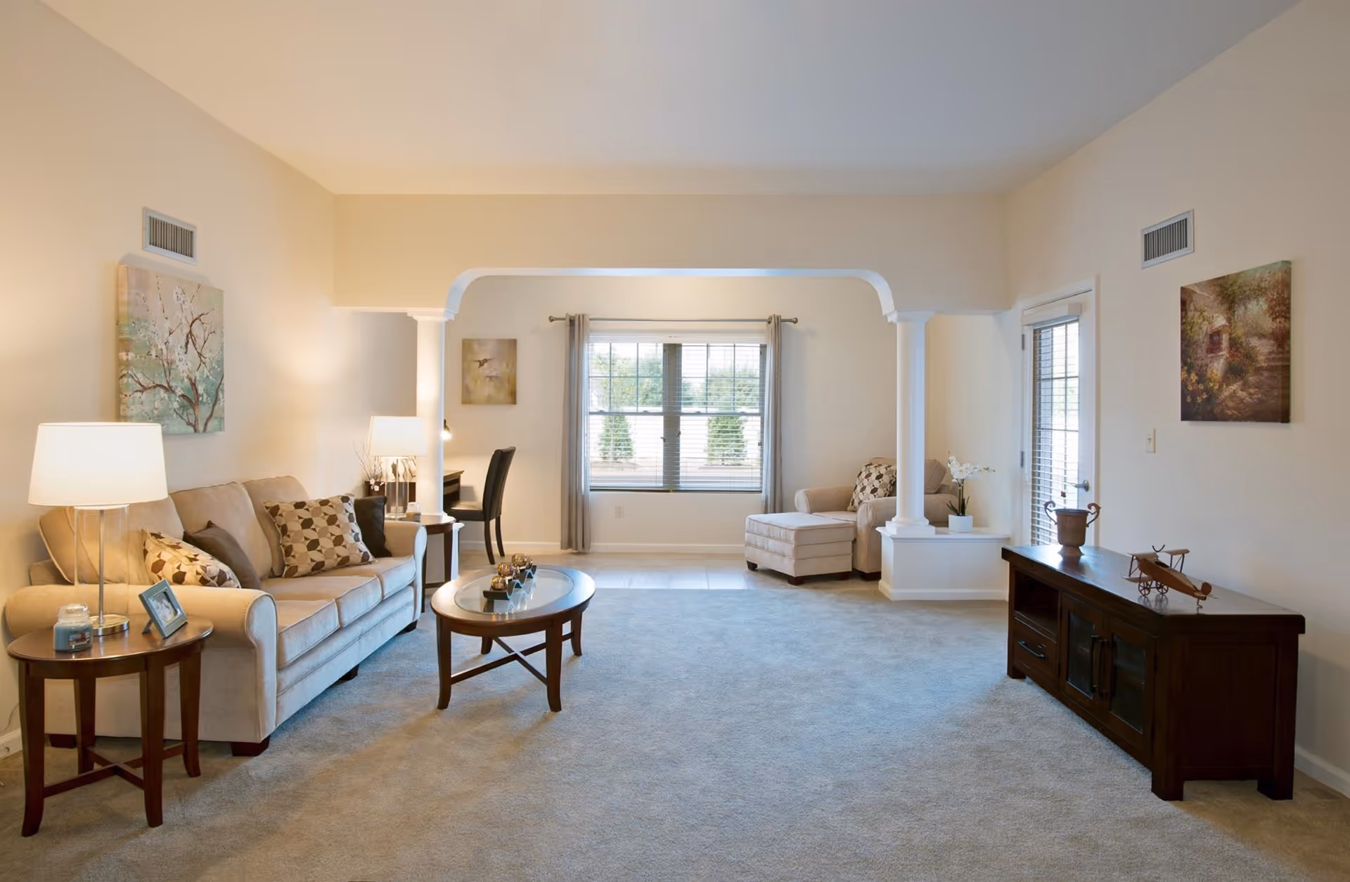 Bright senior living room with beige sofas, lamps, and a center coffee table.