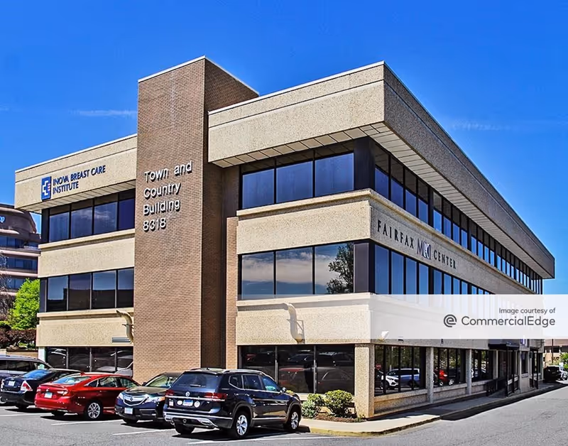 Two-story brick-and-glass office building with a parking lot and blue sky.