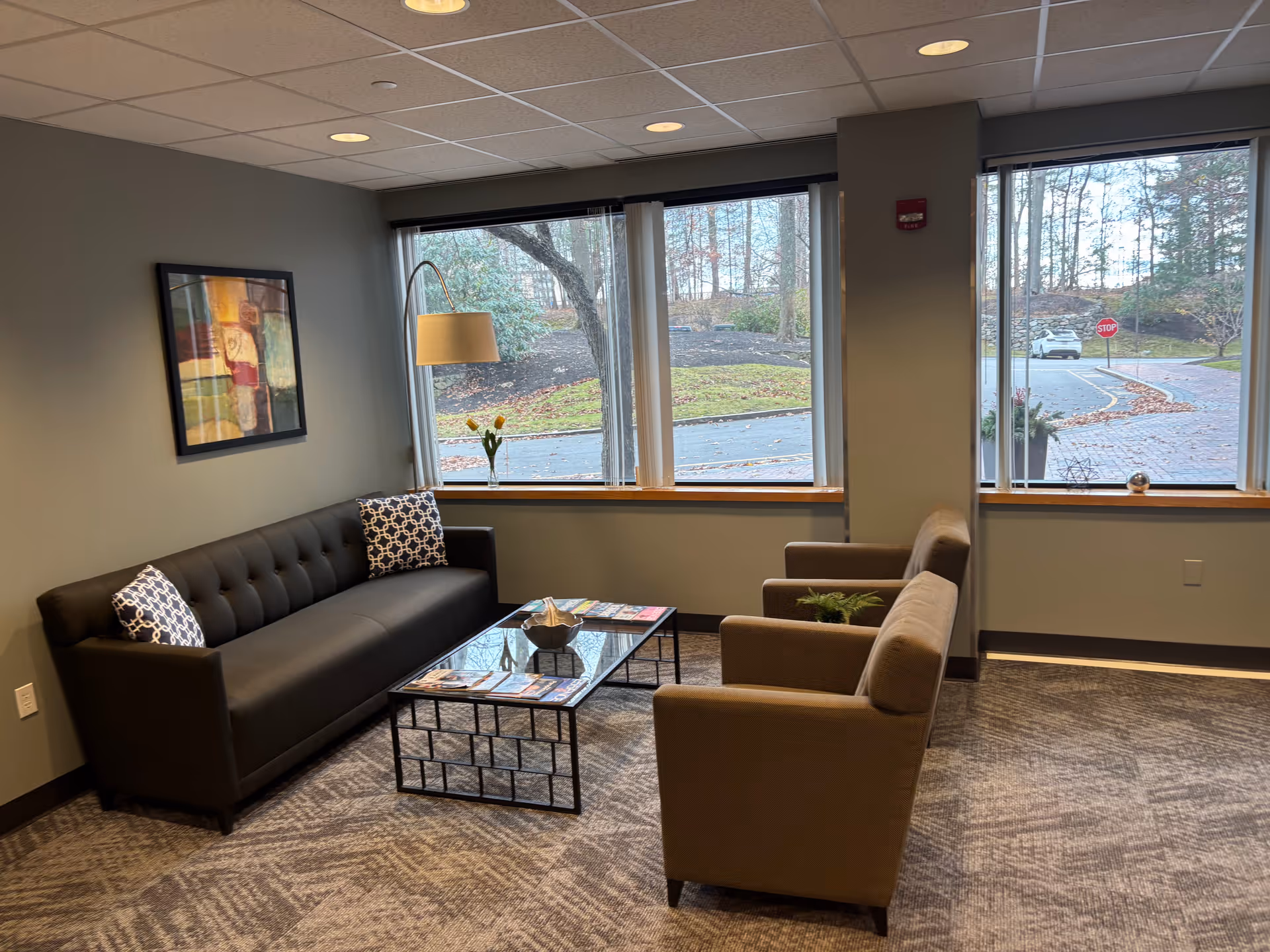 A lounge area with a black tufted sofa, two beige chairs, and a glass coffee table.