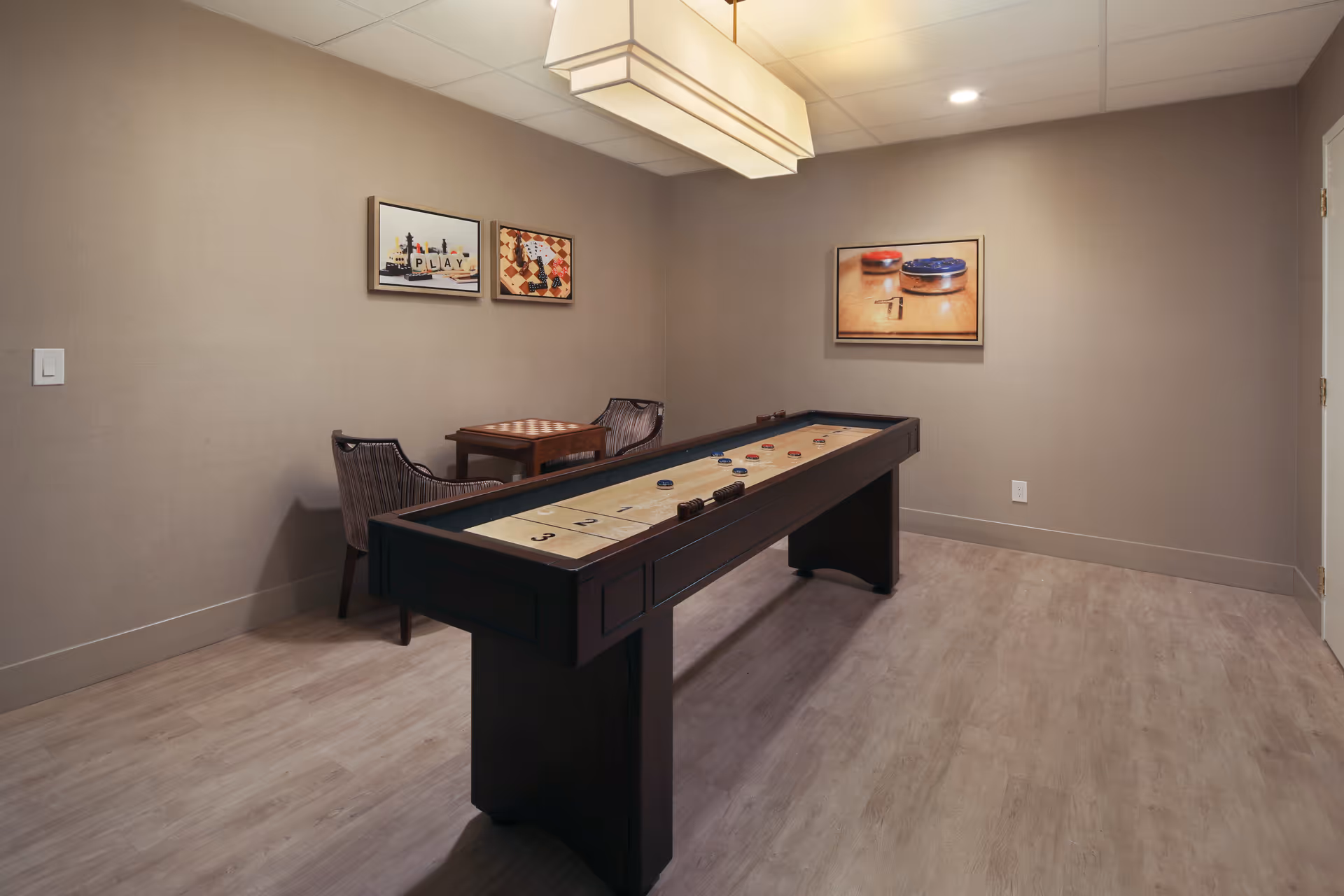Interior recreation room featuring a shuffleboard table, small seating area, and framed wall art.