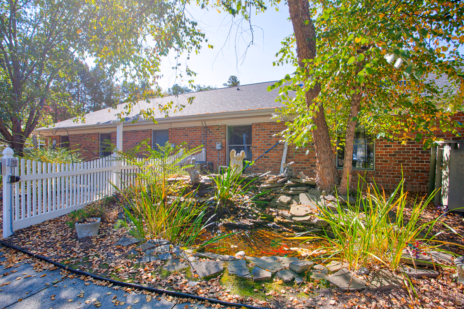 Brick senior living facility exterior with a pond, rocks, and trees in front.