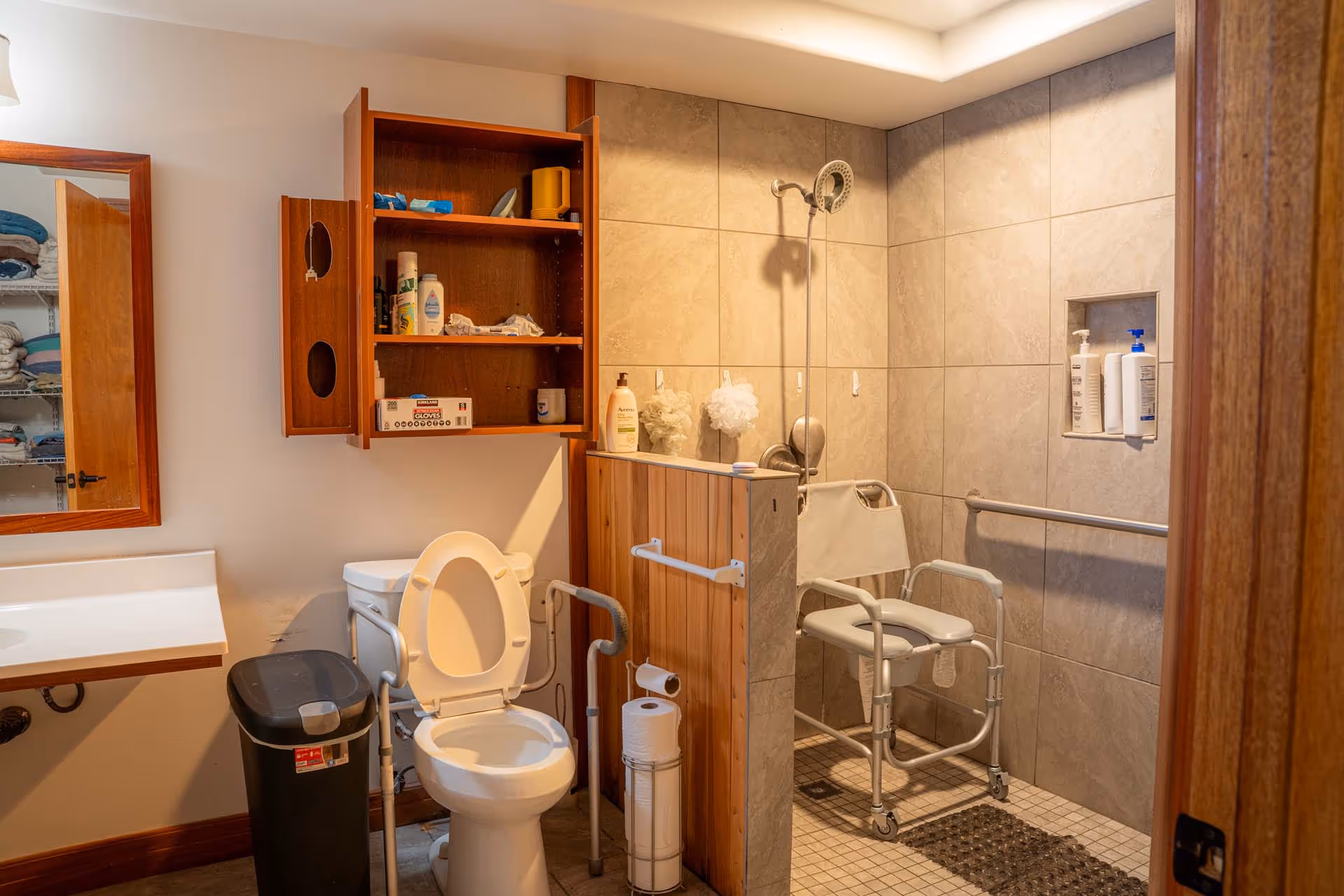 Senior living bathroom with toilet, shower stall, grab bars, and shower chair.
