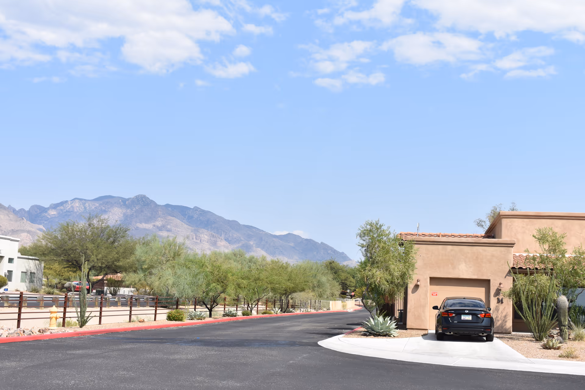Desert road leads to a beige assisted living building with a parked car and mountains.