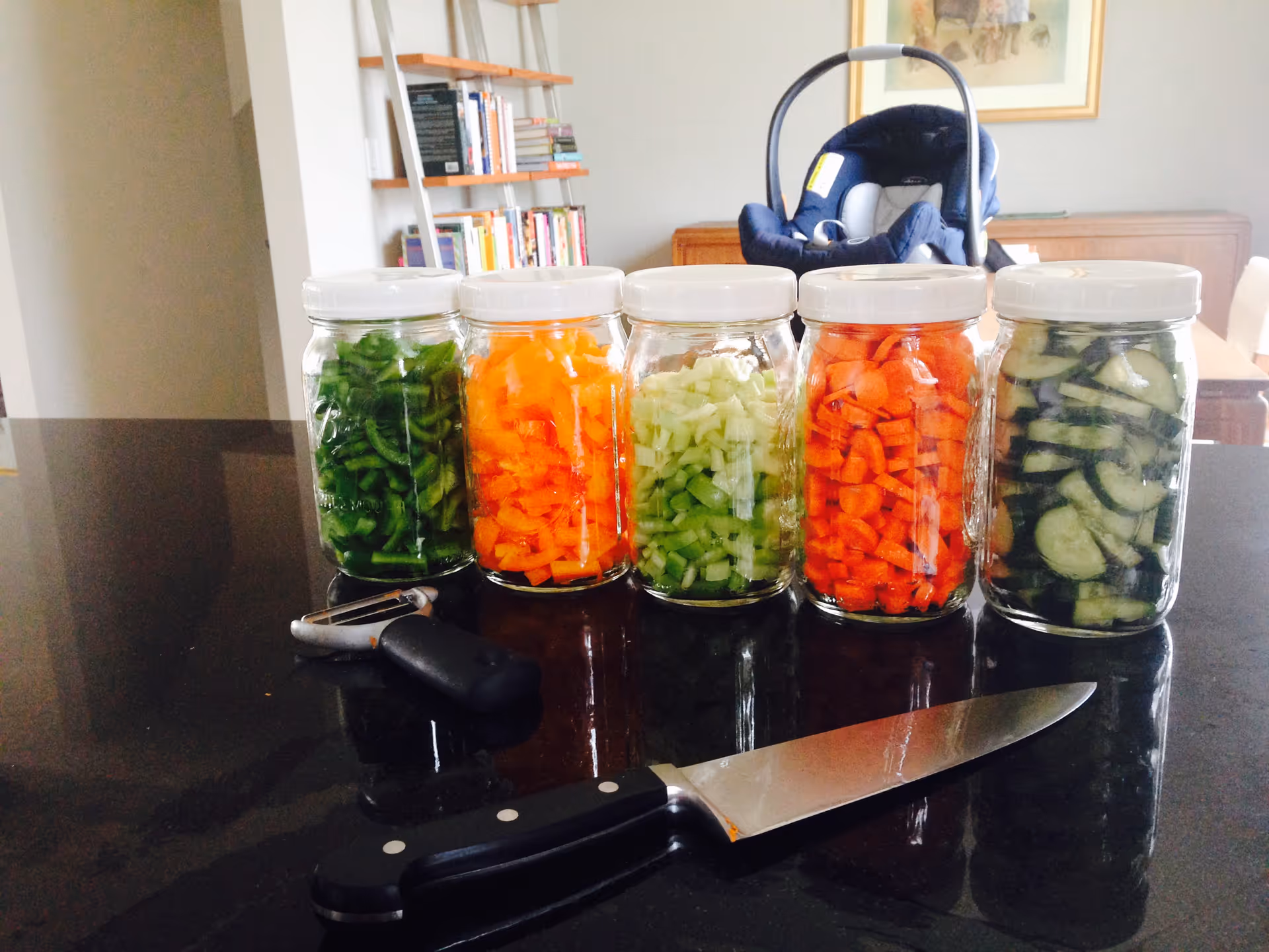 Five glass jars of chopped vegetables lined up on a dark kitchen counter.