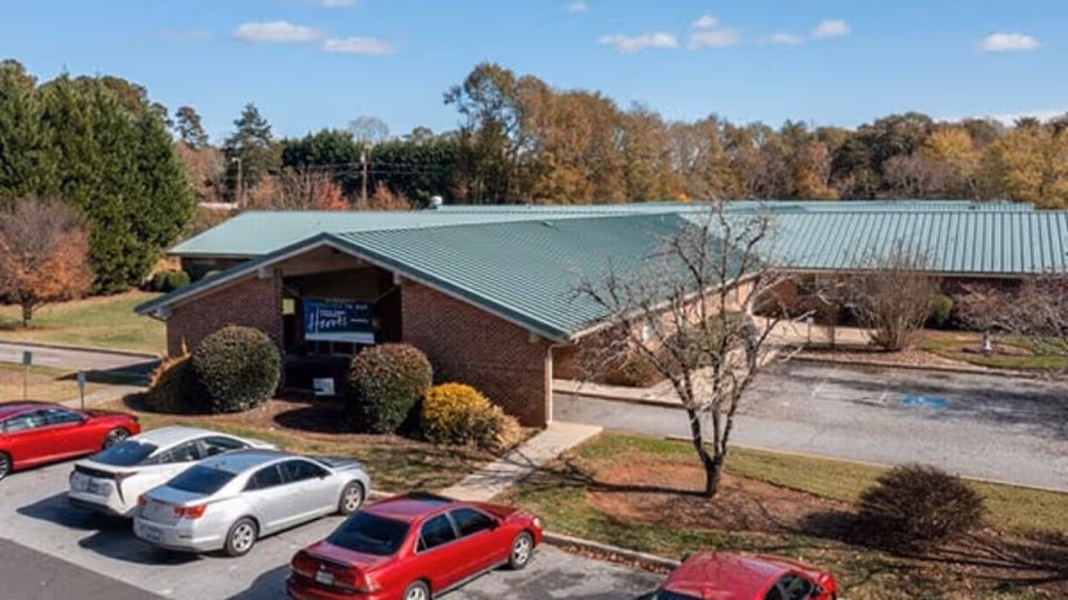 Exterior view of brick facility with green roof and parking lot surrounded by autumn trees