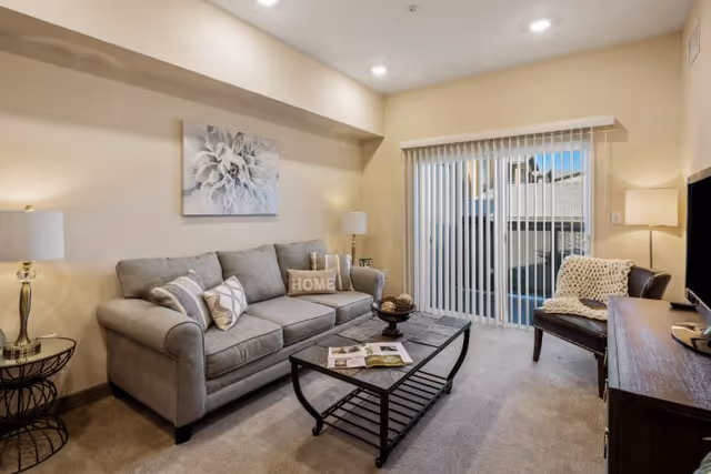 Cozy living room with gray sofa, coffee table, lamps, and sliding glass door.