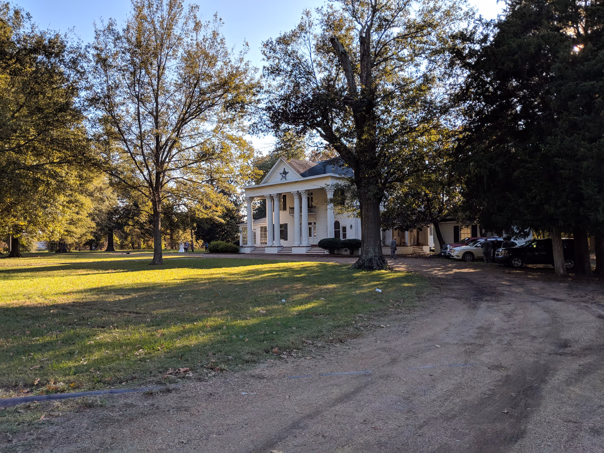 A white, columned front building with a star pediment sits among trees on a grassy lawn.