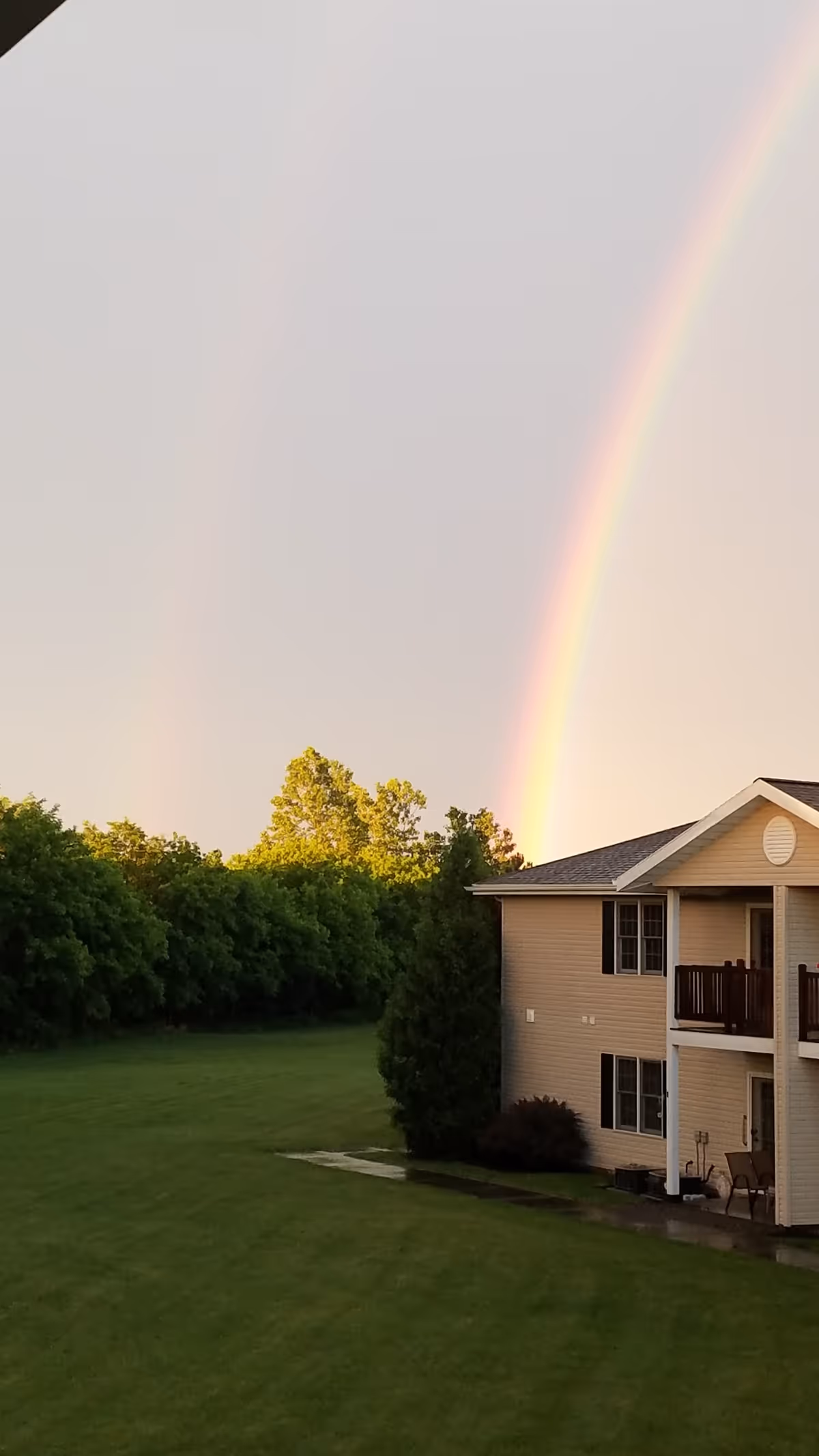 Two-story senior living building with a lush lawn and a rainbow arcing across the sky.