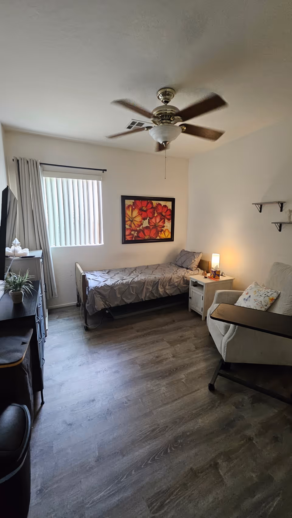 Cozy furnished senior living bedroom featuring a bed, nightstand, sofa, window, and ceiling fan.