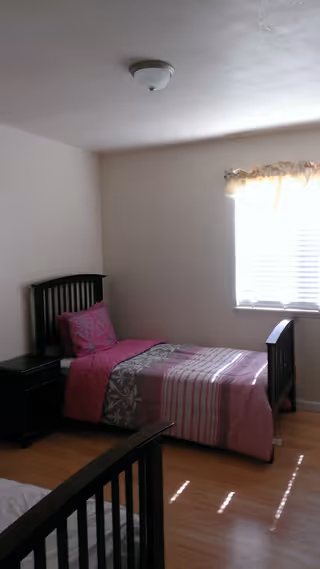 A small bedroom with a single bed, dark wood furniture, and a window with blinds.
